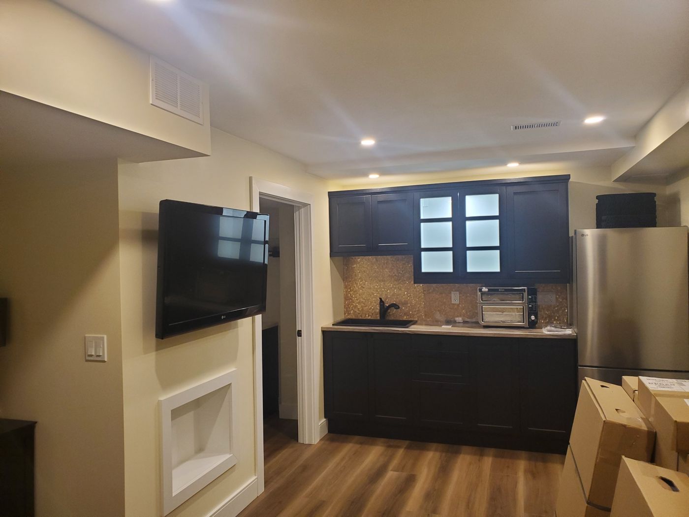 Finished basement with dark cabinets, tile backsplash and pot lights