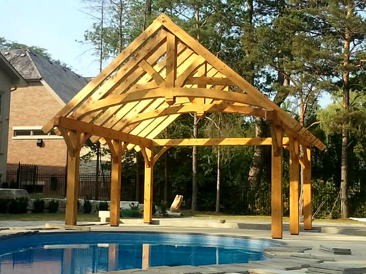 Open timber frame pavilion with curved braces beside a pool